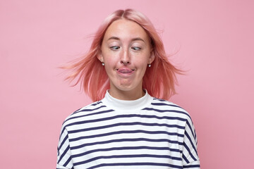 woman with dyed pink hair doing facial expression and touching nose with tongue