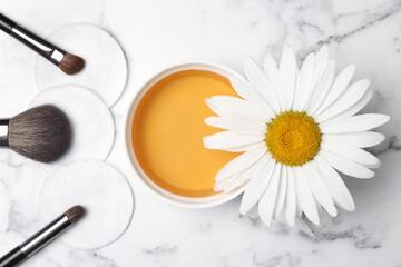 Flat lay composition with chamomile flower and cosmetic product on white marble table