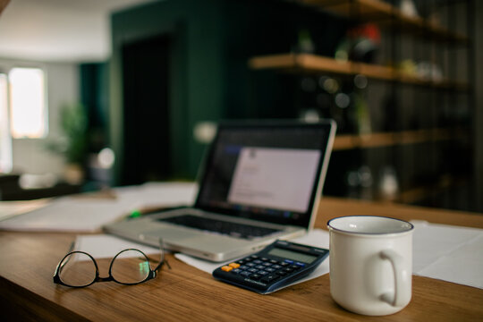 Modern workspace of bookkeeper with netbook on documents and calculator placed on wooden table with eyeglasses and cup of coffee - Powered by Adobe