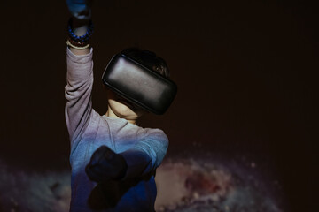 Cute boy wearing VR glasses and exploring virtual reality while standing under colorful projection