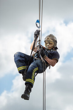 Side view of strong firefighter in protective equipment during training with ropes near building on background of blue sky