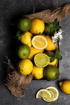 From above view still life of limes and lemons basket placed on dark textured surface