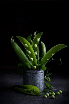 Side view of beautiful composition of peas in a pod placed inside a metallic recipient against a dark background