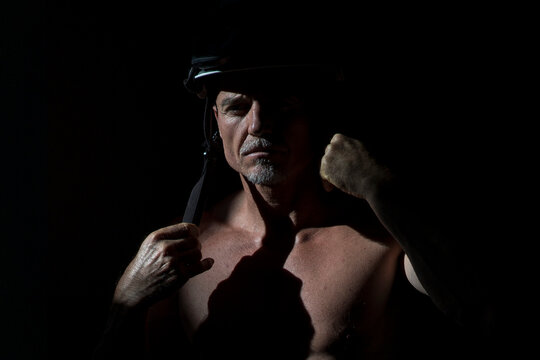 Handsome fireman wearing hardhat and protective respirator during coronavirus pandemic on black background in dark studio looking at camera