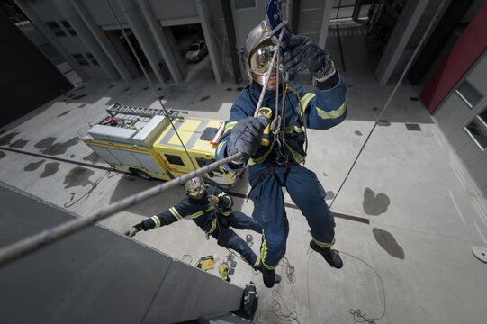 From above of firefighters in protective equipment climbing ropes near building during training