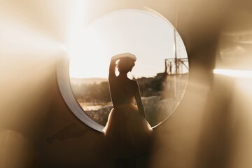 Back view silhouette of anonymous graceful lady in dance costume standing near round hole against blurred nature background and looking away
