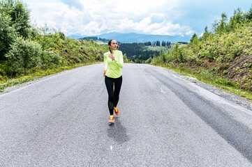 An athletic girl in is running on the road in the mountains. A young woman in trendy sportswear jogging outdoors with a scenic view on the background