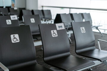 Rows of empty black seats in public waiting area for people with physical disabilities and people with special needs with square white sign demonstrating person on wheelchair