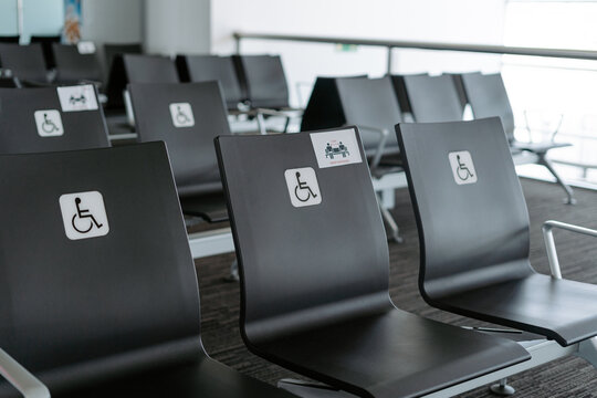 Rows of empty black seats in public waiting area for people with physical disabilities and people with special needs with square white sign demonstrating person on wheelchair