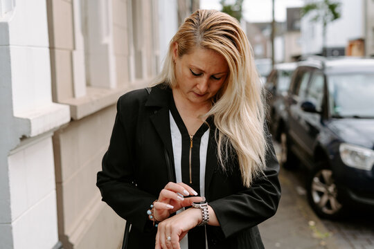 Concentrated female in formal wear walking along pavement sidewalk on street and looking at stylish wristwatch while running late for meeting