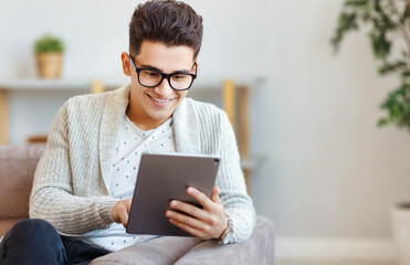 Happy young man using tablet on couch.
