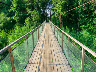 Hanging wooden bridge inside view, against the background of a green forest. Suspension bridge, bridge through the forest, river.