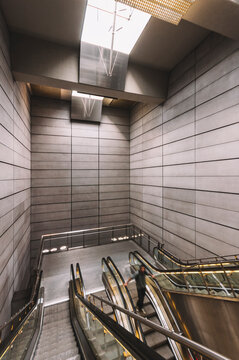 Interior of empty underground with contemporary narrow moving staircase near wall made of rectangles and floor with shiny surface with artificial light on ceiling
