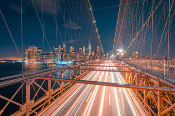 Empty roadway of illuminated Brooklyn bridge at night time with glowing skyscrapers in background in New York City