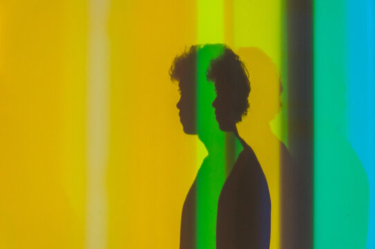 Side view of shadow of young male with curly hair standing in studio with neon lights