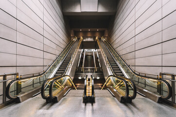 Interior of empty underground with contemporary narrow moving staircase near wall made of rectangles and floor with shiny surface with artificial light on ceiling