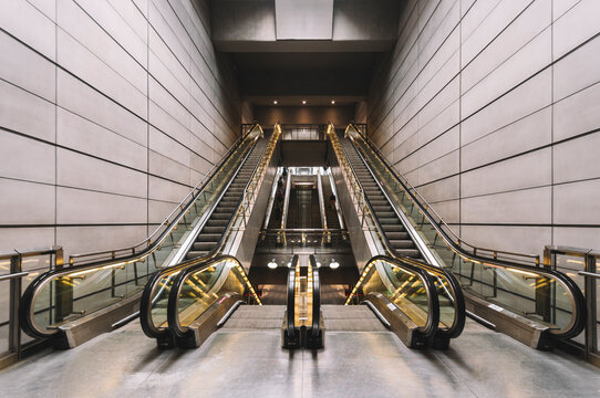 Interior of empty underground with contemporary narrow moving staircase near wall made of rectangles and floor with shiny surface with artificial light on ceiling