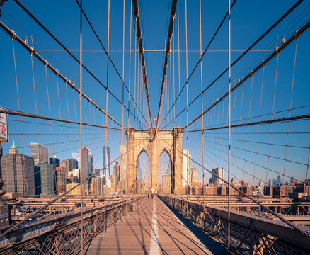 Fototapeta Low angle of pillar of famous Brooklyn bridge crossing river against blue sky with New York cityscape in background in sunny day