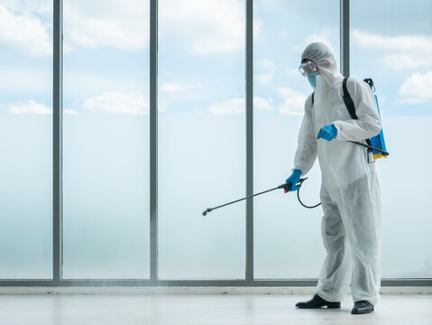 Cleaner man use sterilize spray on company office floor by chemicals sanitizer backpack equipment and wear face mask, transparent goggles, blue gloves and safety uniform to protect bacteria and virus