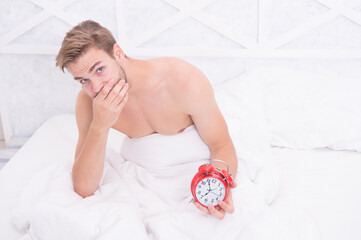 Being late this time. Unhappy man hold alarm clock. Late hours. Sexy guy awake in bed. Morning...