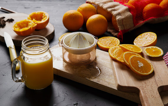 From above composition of halves of fresh oranges on wooden boards and mesh bag near glass jar with orange custard and plastic squeezer