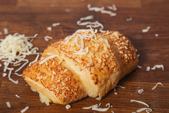 From above of delicious baked croissant with golden crust on wooden table with fresh grated cheese