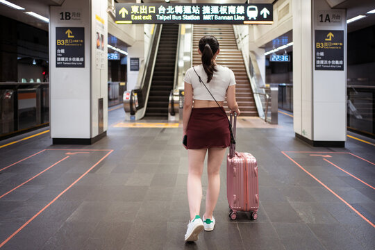 Back view of unrecognizable young female in mini skirt walking with suitcase in railway station while waiting for train