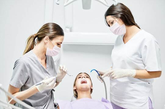 Female client in chair under bright lamp having teeth check up in modern dental clinic
