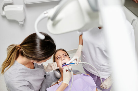 From above of female client in chair under bright lamp having teeth check up in modern dental clinic