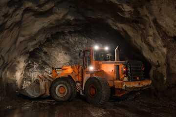 Modern excavator with illuminated headlights placed on dirty soil in underground mine during mining work