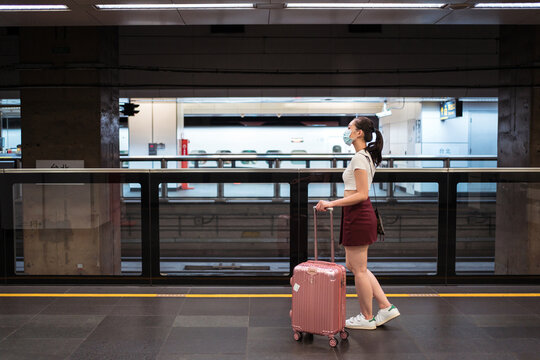 Full length side view young Asian female in mini skirt walking with suitcase in railway station while waiting for train
