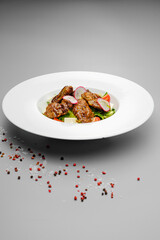 Meat salad with potatoes and grilled vegetables on a white plate.