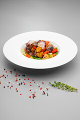 Meat salad with potatoes and grilled vegetables on a white plate.