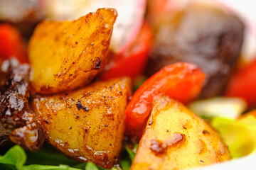Meat salad with potatoes and grilled vegetables on a white plate.