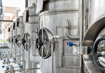 Identical big stainless steel cisterns with metal tubes and fixing pieces of silver color put in row