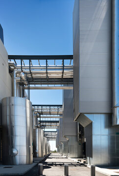 Asphalt walkway going through contemporary factory with metal tanks on background of blue sky