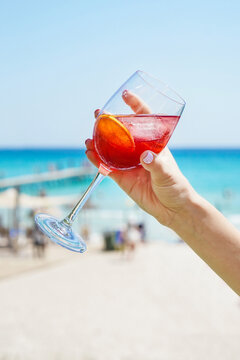 Unrecognizable female holding wineglass of refreshing citrus alcoholic cocktail while chilling on sunny beach in summertime