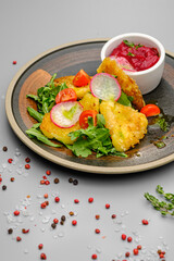 Fried french fries breaded with greens, radishes and beet chips on a white plate.