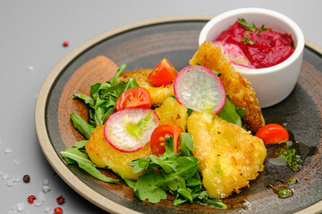 Fried french fries breaded with greens, radishes and beet chips on a white plate.