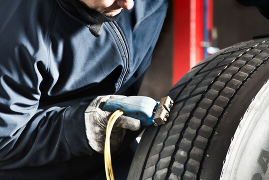 Crop male master in protective uniform using tire regroover while working in garage