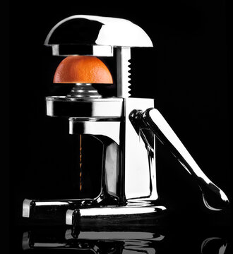 Shiny modern fruit juicer squeezing orange juice on black background in studio