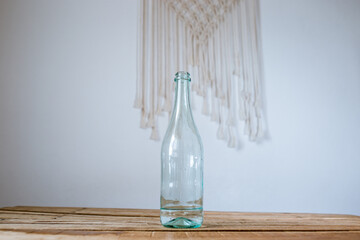 green transparent bottle on a wooden table in the interior with macrame