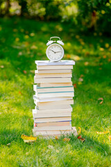 stack of books and an alarm clock on the green grass in autumn