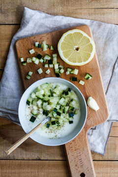 Top view of bowl with delicious cold cucumber and yogurt tarator soup with garlic and lemon served on wooden table