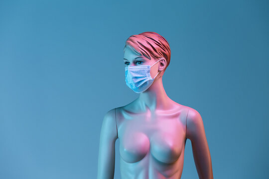Plastic female mannequin in medical mask illuminated by colorful lights in studio on blue background