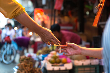 Side view of crop anonymous customer paying with banknote to seller in local street market in Xiamen city in China