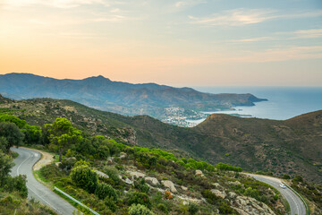 From above of wonderful landscape of sea coast with winding road leading through rocky mountains and green hills near Cadaques town in Spain in summer evening with cloudy colorful sky in background