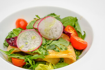 Squid with vegetables, tomatoes, salad and radishes on a white plate.