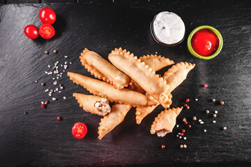Fried fish in batter among spices and sauces on a black stone tray. Fast and ready meal concept