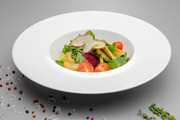 Squid with vegetables, tomatoes, salad and radishes on a white plate.